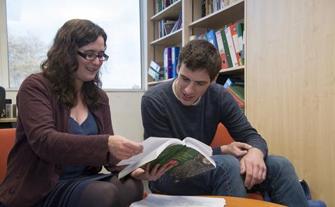 Two students looking at a book in library.
