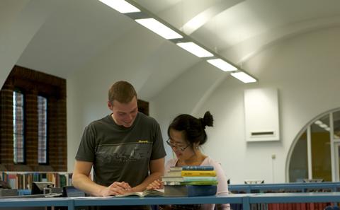 two students stood in the libaray studying a book
