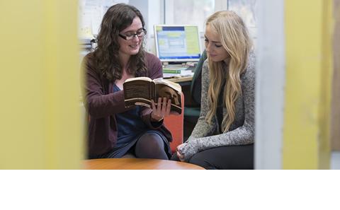 two female students discussing a book together