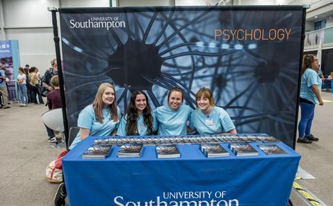 picture of student sat infront of a big poster advertising their programme
