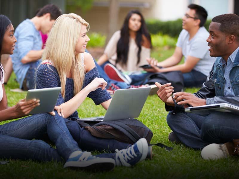 Students with laptops sitting on a lawn