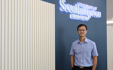 Man standing in front of uni logo