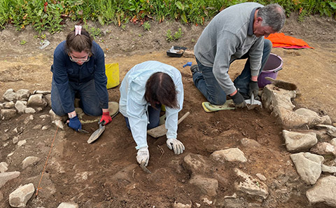 Three people digging in rocky soil.