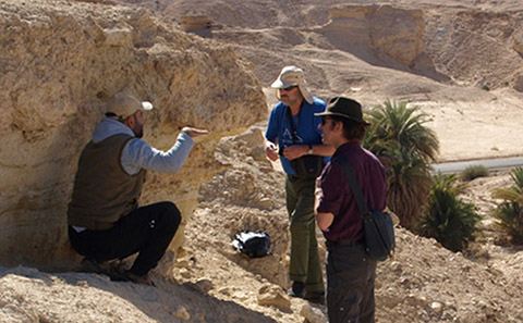 Three researchers in a dry valley conducting fieldwork.