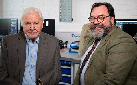 A bearded scientist sits next to Sir David Attenborough.