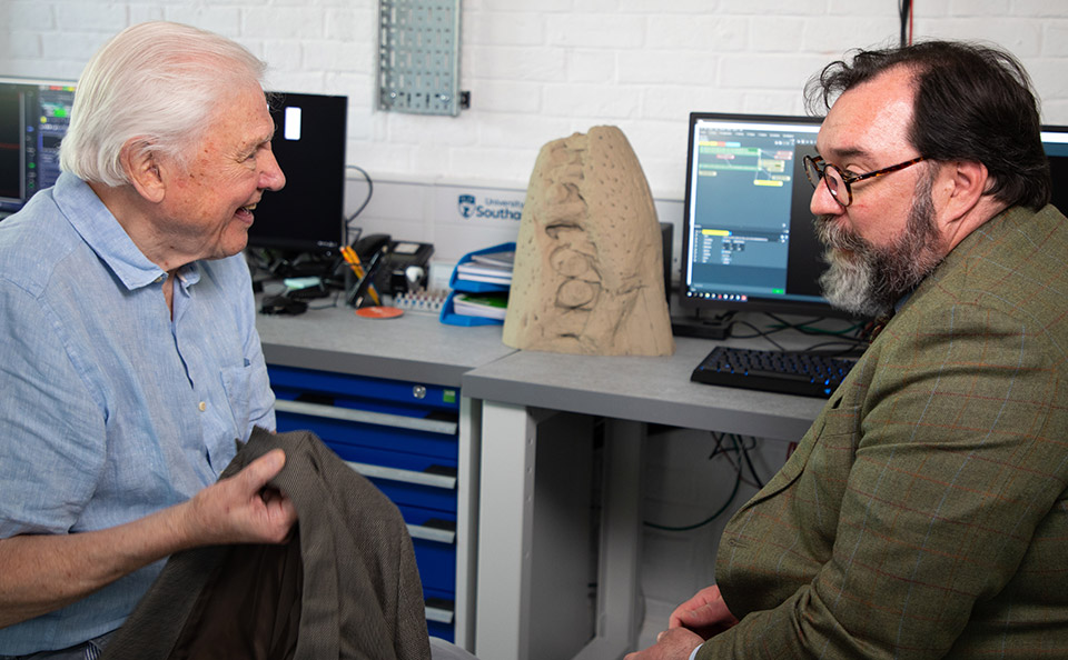 Male scientist with beard dressed in formal jacket speaking to TV presenter Sir David Attenborough