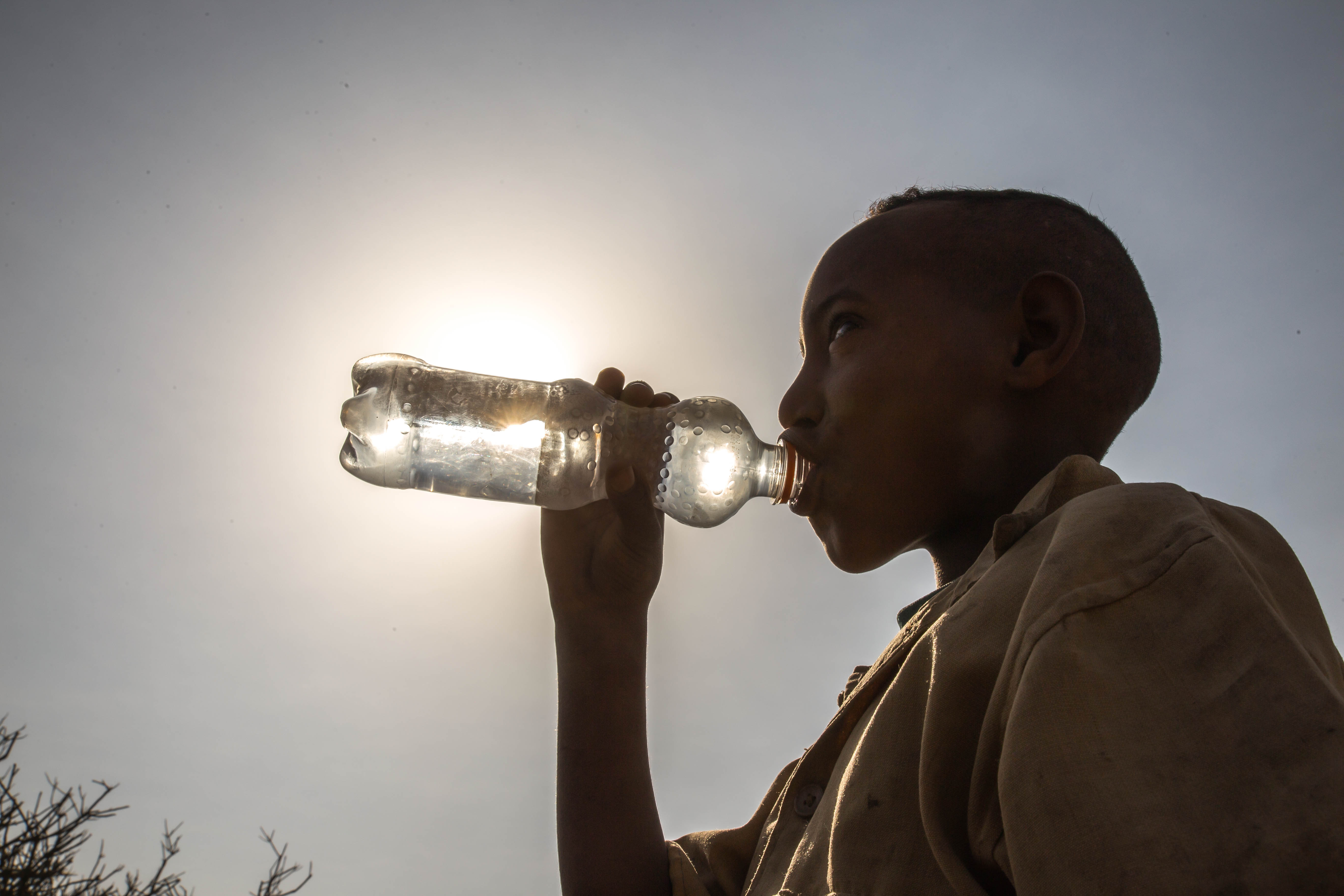 Young african boy drinks water from plastic bottle