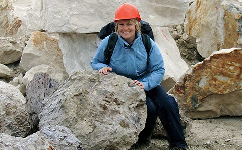 Woman in orange hard hat crouching by rocks
