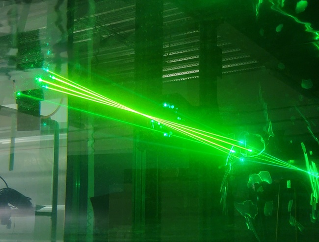 Laser Doppler velocimetry (LDV) system projecting green laser beams through a water tunnel test section