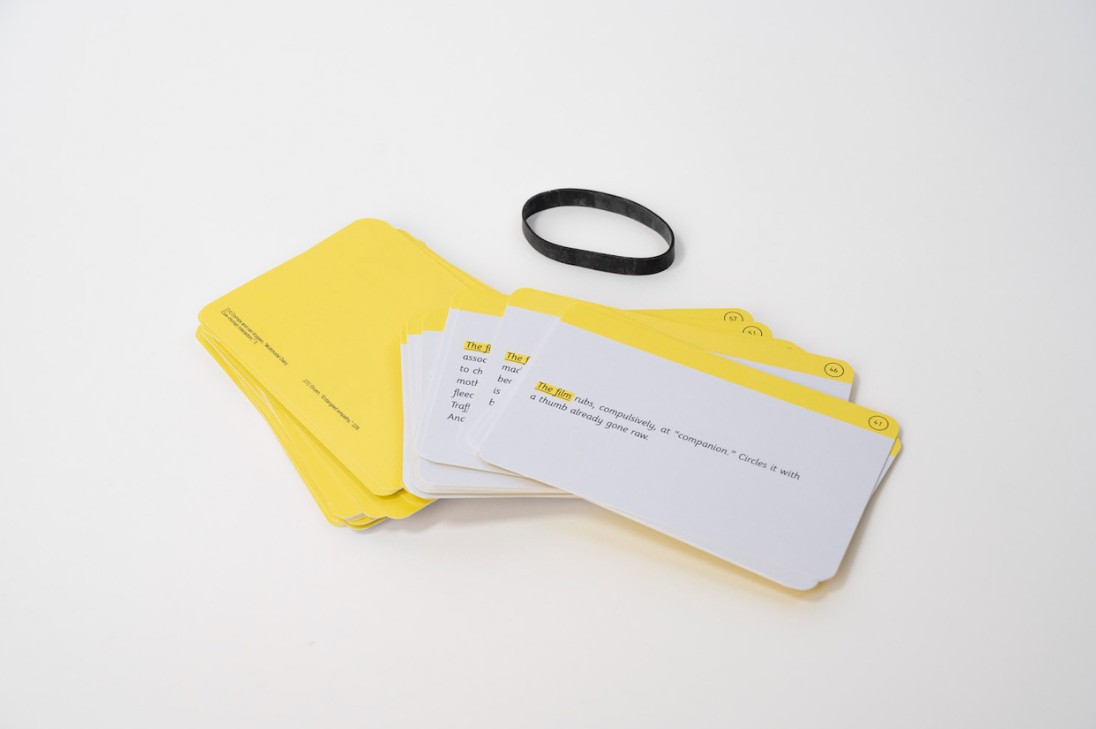A set of yellow and white cards with printed text is spread out on a white surface beside a black wristband-like loop. The minimal design suggests a game, toolkit, or prompt deck.