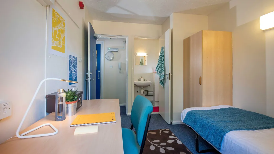 Student bedroom showing bed, desk and entrance to bathroom.