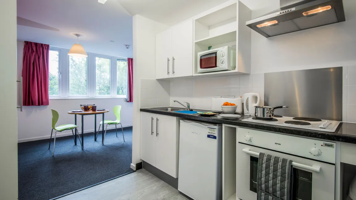 An open plan kitchen area with laminate flooring and modern white kitchen units. A small table, chairs and open window are visible in the background.
