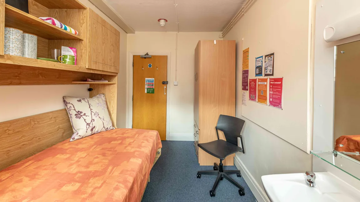 Highfield hall studybed room including bed, wash basin, chair, shelves and cupboards.