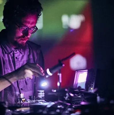 A man with glasses stands over equipment under purple and pink lighting.