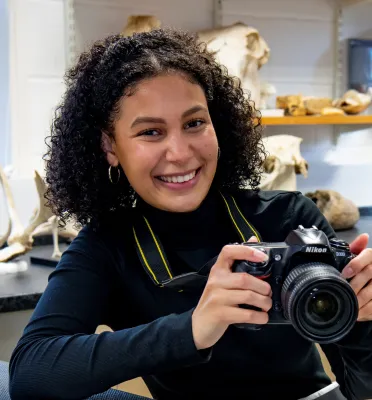 Head and shoulders portrait image of Amber Williams, BA Archaeology and Ancient History Year Abroad student, holding a camera and smiling at the camera.