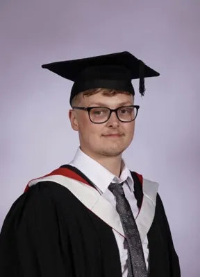 Head and shoulders graduation portrait image of Tommie Bloomfield, MSc Archaeology student wearing a hat and gown, smiling at the camera.