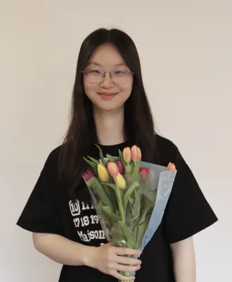Bin Zhang is smiling at the camera and holding a colourful bunch of tulips.
