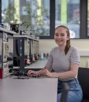 Lydia Moore, MEng Electrical and Electronic Engineering with Industrial Studies student, sitting at an electronics workbench using some testing equipment. 