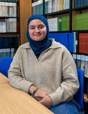 Nora Belkhiter, law student. is sitting at a desk in the law library, smiling at the camera.