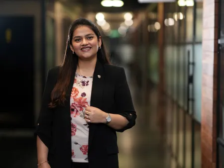MA Luxury Brand Management graduate, Bhavna Sharma, is standing in a corridor smiling at the camera.