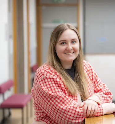 Psychology masters student Katie is leaning on a table and smiling at the camera.