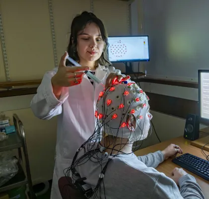 Psychology master’s student Esther is in the lab injecting a colourless liquid into a skull cap. The skull cap, worn by the participant, has bright light and wires attached. 