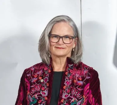A portrait image of Professor Deborah Gill, Vice-President. She's wearing a patterned red jacket and smiling for the camera against a white background. 