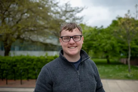 Smiling student wearing glasses standing outside the Physics building..