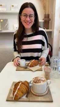 MSc Advanced Clinical Practice student, Chiara, sat in a cafe smiling for the photo. She's sat at a table with a croissant. 