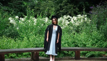 Isabelle, a BSc Pharmacology student, posing for a graduation photo in front of vibrant green foliage and white flowers. 