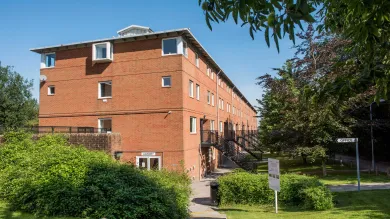 Exterior view of three storey red brick accommodation building surrounded by grass and trees.