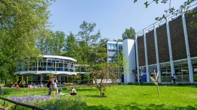 Modern looking campus building with, students relaxing on a grassy area in the foreground.