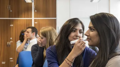 Several students in partner groups, inspecting each others' ears with an otoscope.