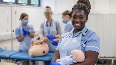 A midwifery students hold a baby manikin as students practice their clinical skills