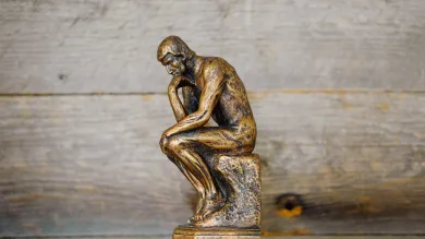 A small replica of 'The Thinker' - a bronze sculpture by Auguste Rodin depicting a man hunched over on a rock in contemplation - set against a backdrop of wood panels.
