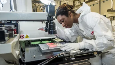 A PhD student leaning over to carefully observe a sample of printed electronics in the lab.