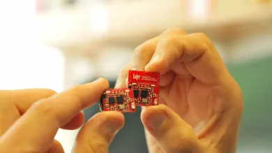 Hand holding a red internet of things circuit board created by the Centre for IoT and Pervasive Systems. 