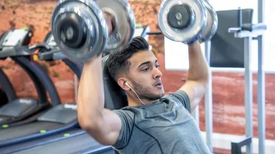 A student lifts weights above his head, he looks determined