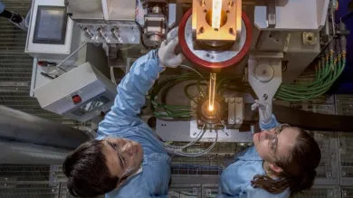 View from above of two researchers feeding glass into a fibre drawing furnace.