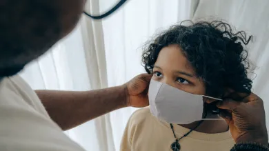 A patient looks up as a medical professional puts a clinical mask onto them