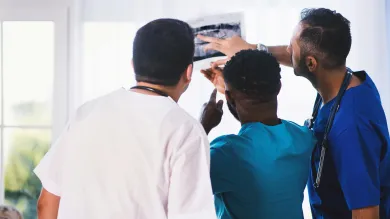Three healthcare professionals examining an X-ray next to a window.