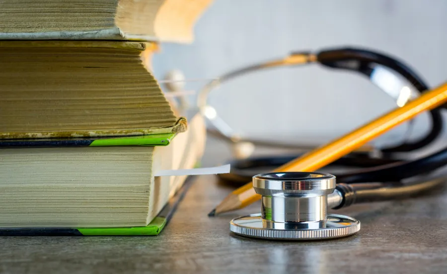Stack of books with a stethoscope and pencil in front.