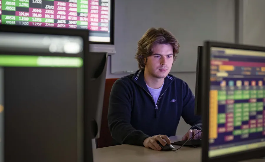 A student working at a computer surrounded by screens displaying colourful data tables.