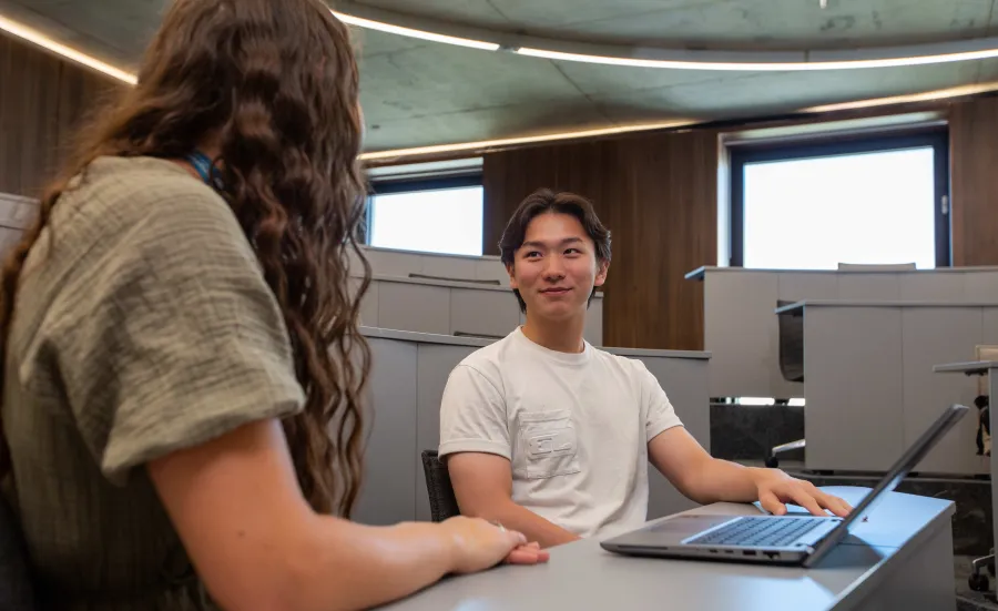 Student speaking with a careers adviser while using a laptop in a campus study space.