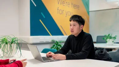 Student using a laptop during a one-to-one careers support conversation in a campus space.