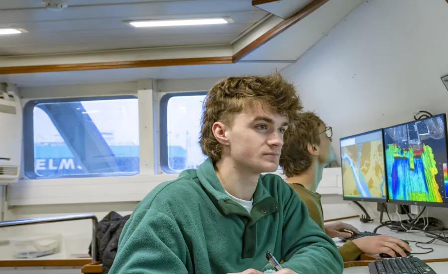 Students on the research vessel looking at screens showing colour-coded visual data of seabed mapping.
