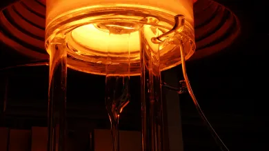 Glowing furnace with glass rods extending downward, emitting orange light.