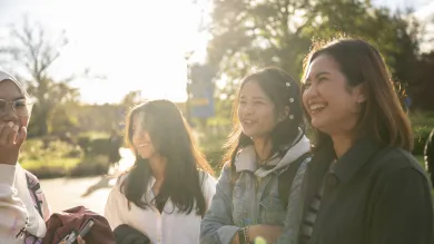 A group of students on a sunny day standing and chatting to each other with a smile. 