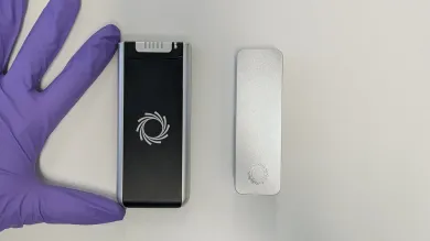 Two Oxford Nanopore MinION portable DNA sequencing devices shown on a laboratory bench beside a gloved hand for scale.