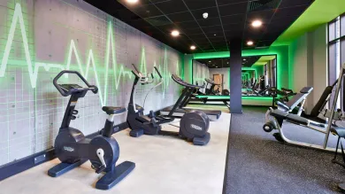 The gym at Southampton Crossings features exercise bikes and treadmills. It's a well-lit space with decorative green neon lighting on the walls and a large mirror at the back. 